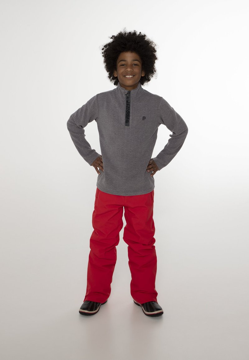 Grijze longsleeve pullover met een halve rits kraag, rode sneeuwbroeken en zwarte schoenen. De pullover heeft een logo op de borst.