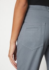 Pantalones de mezclilla gris con un diseño ajustado, que muestran un bolsillo trasero y detalles de costura; textura suave y sutiles variaciones de color.