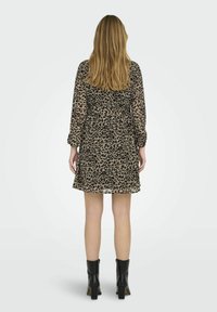 Krátky rukáv, šaty s leopardím potlačou v béžovej a čiernej farbe, s priliehavým pásom a rozšírenou sukňou, doplnené čiernymi členkovými čižmami.