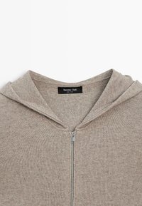 Hellbrauner Kapuzenpullover mit Reißverschluss und weicher Textur, ausgestattet mit einer Kordelzugkapuze, gerippten Kanten und einem Metallreißverschluss. Das Etikett trägt die Aufschrift "Massimo Dutti".