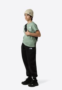 Pamut póló menta zöld színben, fekete polárnadrág, fekete sportcipő és bézs kötött sapka, válltáskával és látható logókkal.