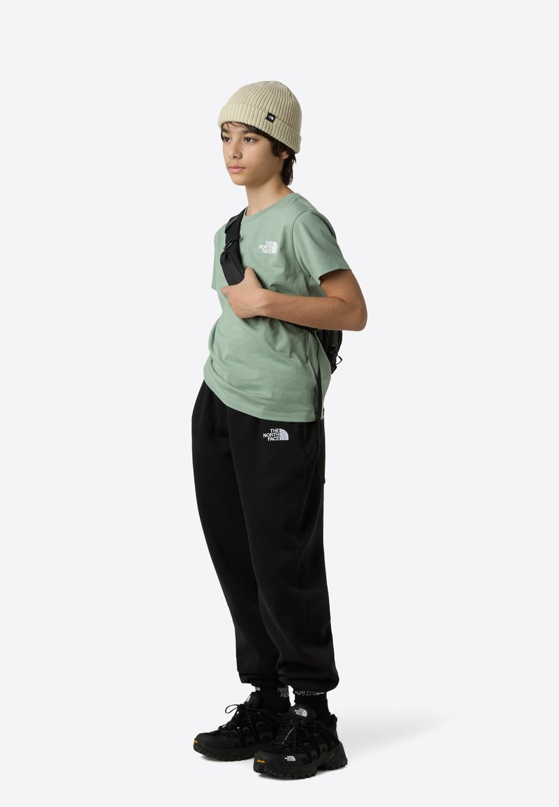 Pamut póló menta zöld színben, fekete polárnadrág, fekete sportcipő és bézs kötött sapka, válltáskával és látható logókkal.