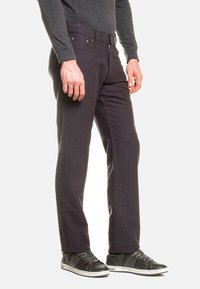 Pantaloni dritti grigio scuro in cotone, con zip, tasche laterali e dettagli cuciti, abbinati a sneakers nere.