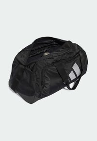 Svart duffelbag med teksturert nylonmateriale, glidelås, side mesh-lomme og en stor grå logoakcent på den ene siden.