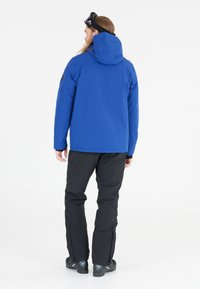 Giacca isolante blu con cappuccio, pantaloni da sci neri e calzature nere. Tra le caratteristiche ci sono un design elegante e dettagli semplici e funzionali.