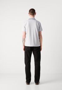 Polo grigio chiaro con colletto, maniche corte e bordatura scura, abbinato a pantaloni neri e scarpe marroni. Mostra uno stile semplice e casual.