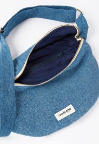 Sac à épaule en denim bleu avec fermeture éclair. À l'intérieur, il y a une doublure en tissu foncé et une poche zippée. L'étiquette affiche le logo "rive droite".