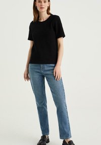 Czarny krótki sweter z rękawami, zestawiony z jasnoniebieskimi dżinsami o prostym kroju i czarnymi loafersami. Gładka faktura, swobodny krój, klasyczny design.