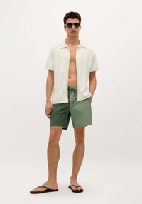 Korte mouw crème shirt met knopen, groene short en zwarte slippers; gladde texturen en een eenvoudig ontwerp.
