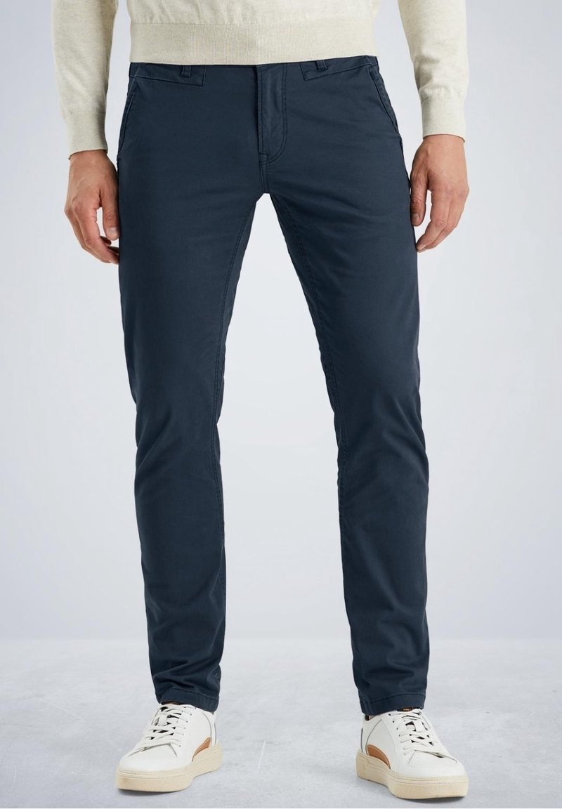 Slim-fit, marineblauwe chinos gemaakt van lichtgewicht katoen. Voorzien van voorzakken, riemlussen en een soepele textuur. Gekleed met witte sneakers.