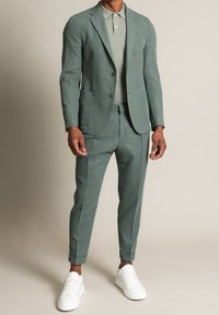 Dwuczęściowy garnitur z teksturowanej, jasnozielonej tkaniny o dopasowanym kroju. Połączony z jasnozieloną koszulką polo i białymi sneakersami.