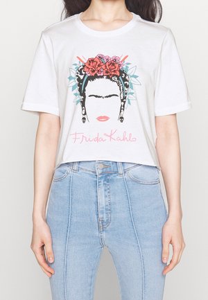 Valkoinen puuvillainen t-paita, jossa on graafinen painatus naisen kasvoista, jotka on koristeltu kukilla, mustista hiuksista, ja teksti "Frida Kahlo" vaaleanpunaisena.