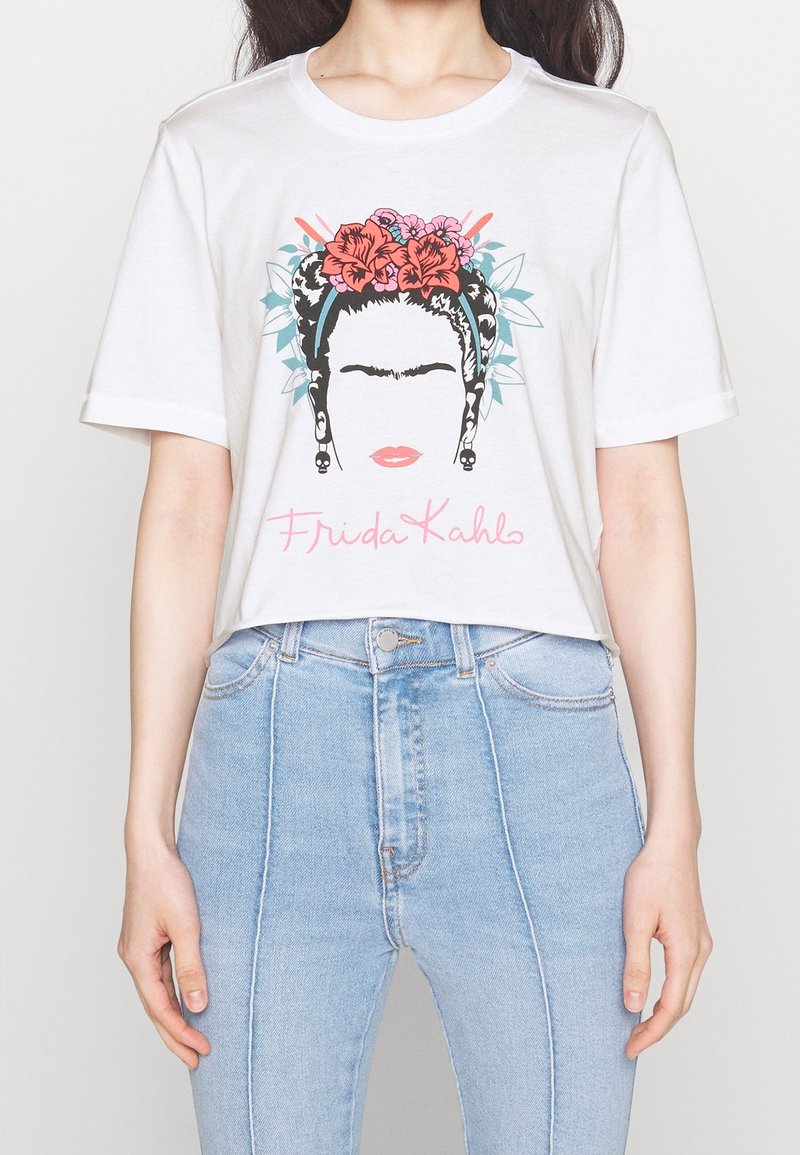 Bílý bavlněný tričko s grafickým potiskem tváře ženy zdobené květinami, s černými vlasy a textem "Frida Kahlo" v růžové barvě.