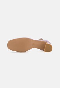 Chaussure à talon avec un dessus lilas, texture lisse et semelle en caoutchouc beige. Présente un talon arrondi et une marque discrète sur la semelle.