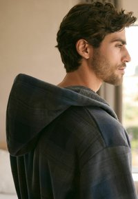 Herren-Karohoodie in dunklen Tönen, weicher Stoff mit strukturiertem Innenfutter, ausgestattet mit einer drapierten Kapuze und lockerer Passform.