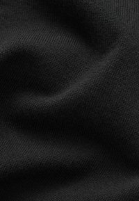 Tissu tricoté noir avec une texture visible et des plis doux créant des ombres légères sur la surface.