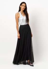 Zilveren mouwloze top met een glanzende afwerking, gecombineerd met een luchtige zwarte tule maxi rok met een aansluitende tailleband en gelaagde textuur.