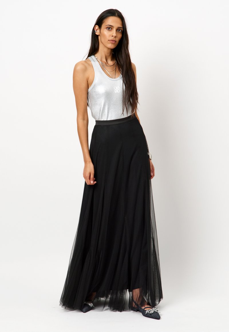 Zilveren mouwloze top met een glanzende afwerking, gecombineerd met een luchtige zwarte tule maxi rok met een aansluitende tailleband en gelaagde textuur.