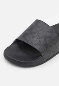 Sandalia negra de slide con parte superior texturizada que presenta un patrón sutil, suela de goma, tira ancha y acabado suave.