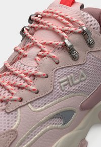 Κοντινή λήψη ροζ αθλητικού υποδήματος FILA με κορδόνια σε ροζ και άσπρο μοτίβο, μεταλλικά αστερίσκια, υφές από δίχτυ και δέρμα, και λεπτομέρειες σε χοντρή σόλα.