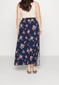 Jupe maxi fleurie en marine avec des fleurs roses et blanches, dotée d'une taille ajustée et d'une fente sur le côté pour plus de liberté de mouvement. Texture de tissu douce.