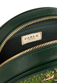 Runde grüne Ledertasche mit goldenem Reißverschluss, Polyesterfutter und einem Innenlabel. Verziert mit gesticktem Laub und Fischen.