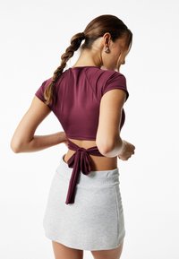 Top corto de color marrón con un diseño atado en la espalda, combinado con una mini falda de color gris claro. La tela parece suave y elástica.