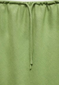 Hellgrüner Stoff mit einem elastischen Bund und einem dünnen Kordelzug, der in der Mitte herunterhängt.