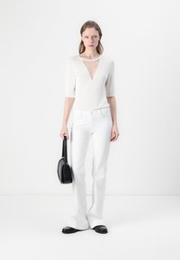 Haut en maille légère blanc avec un décolleté en V plongeant ; associé à un jean flare blanc ajusté. Accessoirisé avec un petit sac à main noir.