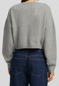 Suéter gris recortado con un tejido suave y texturizado, acompañado de unos vaqueros de mezclilla oscuros que presentan un diseño de bolsillo clásico.