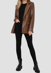 Brown faux leather blazer with peak lapels, single button closure, and front pockets, paired with black fitted pants and ankle boots.