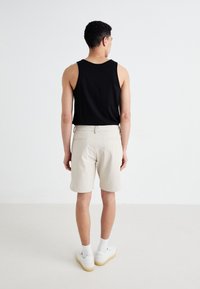 Svart ermeløs tanktop kombinert med lysebeige shorts. Shortsene har flat front, lommer og en skreddersydd passform. Hvite sneakers fullfører antrekket.