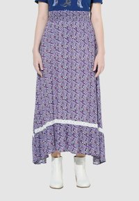 Gonna maxi floreale viola con un accento in pizzo all'orlo, caratterizzata da un design fluido e abbinata a stivaletti bianchi alla caviglia.