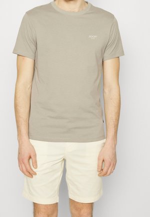 Camiseta de algodón beige claro con cuello redondo y mangas cortas. Presenta un pequeño logo impreso en el pecho izquierdo. Combinada con pantalones cortos blancos.