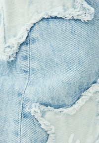 Tejido de mezclilla azul claro con parches en forma de estrella deshilachados y costuras visibles.