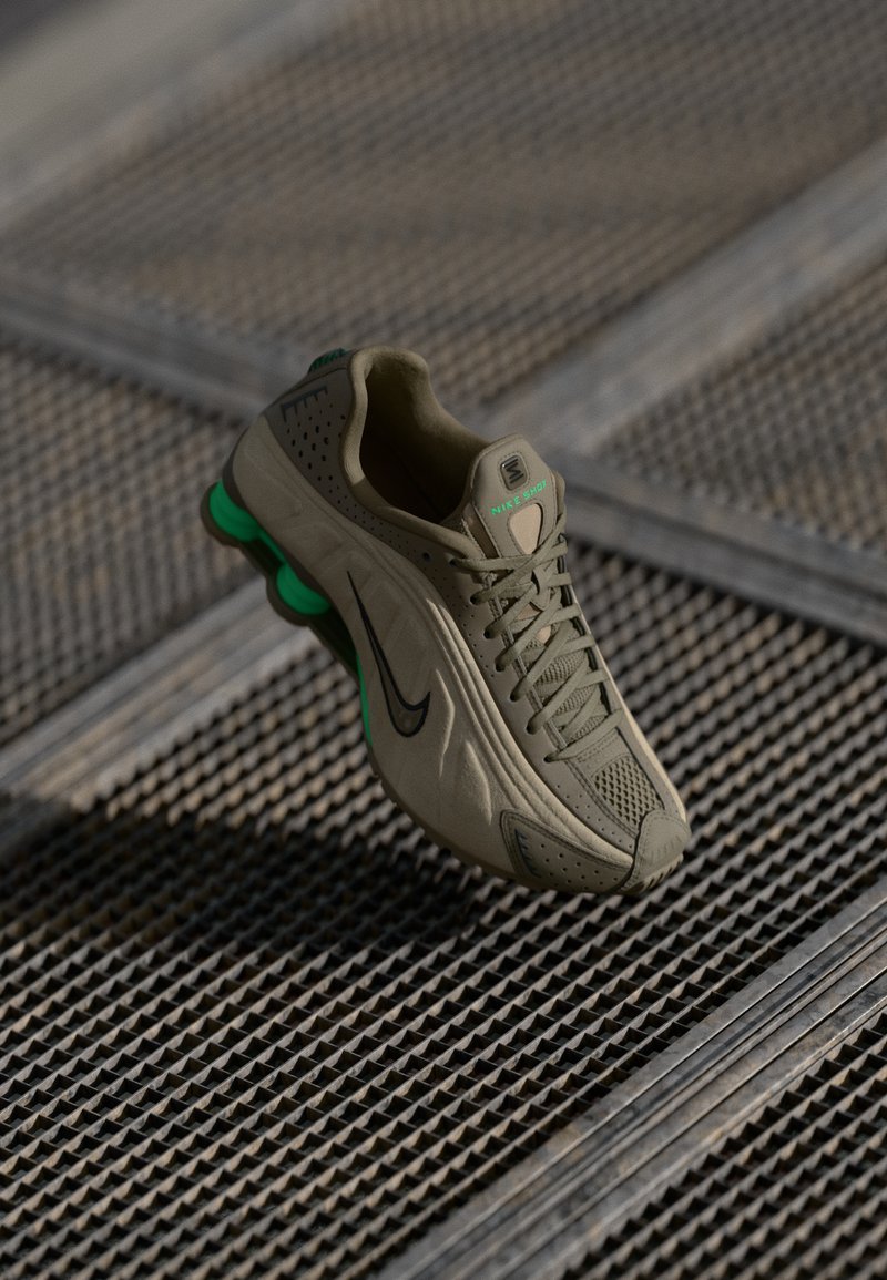 Baskets de course Nike en vert olive avec une tige perforée, logo noir, accents verts et une semelle rembourrée, présentées au-dessus d'une surface texturée.