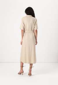 Abito midi beige con maniche corte, vita con cinturino e taglio dritto. Abbinato a tacchi a strappo marrone chiaro. Tessuto liscio, dettagli minimi.