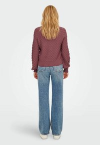 Lila gestepptes Sweatshirt mit gerippten Bündchen und Saum, kombiniert mit hellblauen weiten Jeans und weißen Sneakern, von hinten betrachtet.