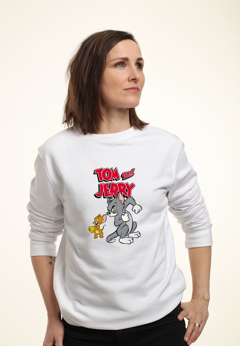 Hvid sweatshirt med et grafisk print af Tom og Jerry. Designet inkluderer farverige illustrationer med rød tekst, der læser "TOM og JERRY."