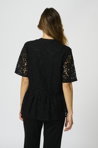 Top in pizzo nero con maniche corte, design peplum, motivo floreale, tessuto testurizzato, scollatura rotonda e schiena scoperta. Abbinato a pantaloni neri.