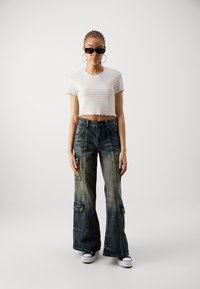 Top corto bianco a costine con orlo scallop abbinato a jeans cargo blu scuro a gamba larga con molteplici tasche e leggero effetto sbiadito, indossato con sneakers nere.