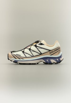 Μπεζ και λευκό παπούτσι Salomon για τρέξιμο σε μονοπάτια με μαύρες γραμμές, σύστημα ταχείας δέσης και μπλε-λευκή σόλα, εμφανίζεται σε ουδέτερο φόντο.