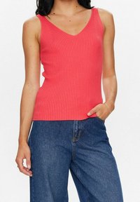 Korallfärgad ribbad linne med V-ringning, figurnära design och breda axelband, kombinerad med mörkblå vida jeans.