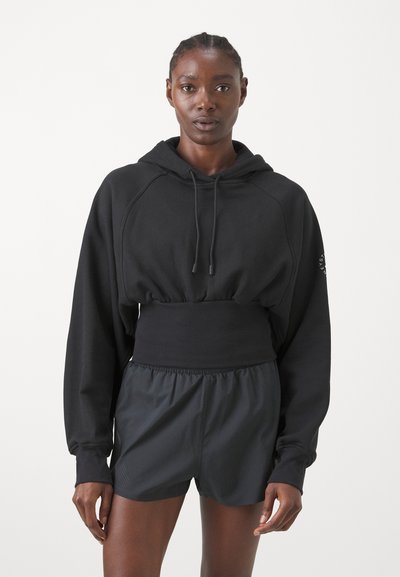 Felpa corta nera con vita a coste e lacci; abbinata a pantaloni da corsa neri con vita elastica.