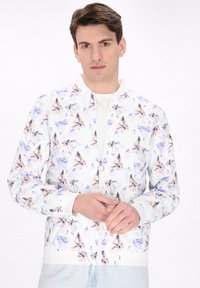 Witte bomberjack met een geometrisch patroon van pastelgekleurde driehoeken en palmbomen, met een rits en geribbelde manchetten.