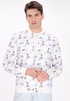Witte bomberjack met een geometrisch patroon van pastelgekleurde driehoeken en palmbomen, met een rits en geribbelde manchetten.