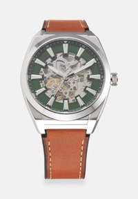 Montre-bracelet pour homme avec boîtier argenté, cadran vert montrant des engrenages mécaniques, index blancs en gras et bracelet en cuir marron avec coutures blanches.