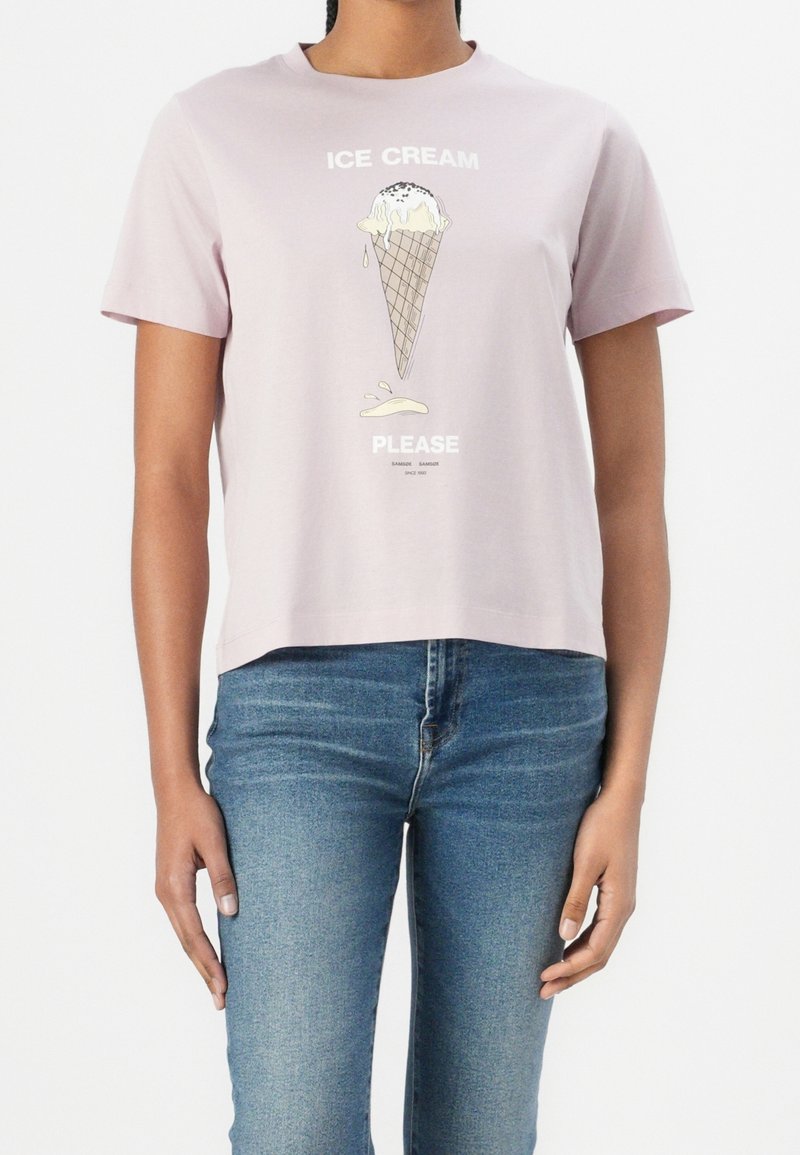 Femme portant un t-shirt rose clair avec un motif cornet de glace fondant et le texte « ICE CREAM PLEASE », assorti à un jean bleu.