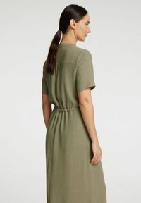 Robe à manches courtes, couleur olive, avec une taille élastique, présentant un détail de patte de boutonnage au dos et une texture de tissu lisse et léger.