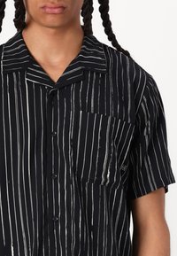 Short-sleeve black shirt with white vertical stripes, soft fabric, pointed collar, and a chest pocket. Buttons in front.